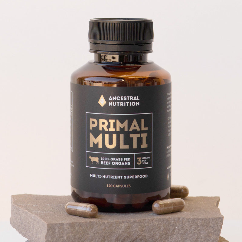 A bottle of Primal Multi Beef Organ freeze dried capsules placed on a slate with loose capsules by Ancestral Nutrition